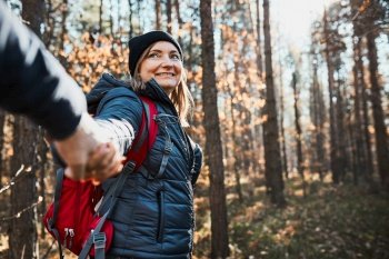 Couple holding hands enjoying trip while vacation day Hikers with backpacks walking on forest path on sunny day Active leisure time close to nature