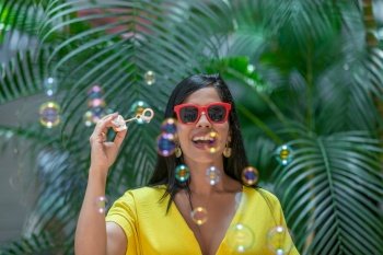 Front view of a cheerful Latina woman with bubbles in the air against a background of green plants outdoors Cheerful Latina woman with bubbles in th