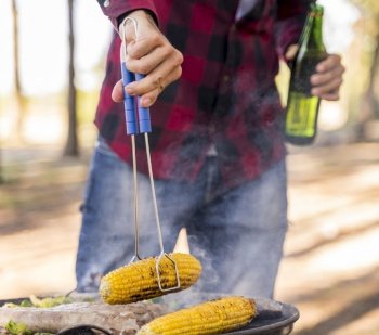 man roasting corn barbecue while drinking beer