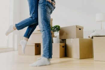 Faceless young couple move in new home  man lifts woman  have fun  surrounded with unpacked cardboard boxes  start new life in recently bought abode 