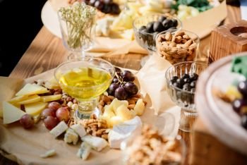 Different kinds of cheese with wine  figs  walnuts  ham  grapes  honey  toast In a rustic style Cheese set on a plate laid out on a beige backgroun