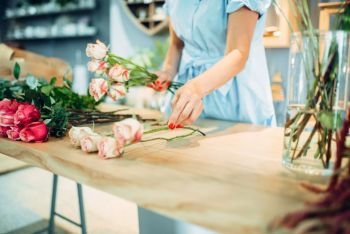 Female florist makes rose composition on the table in flower shop Floral artist making bouquet at the workplace