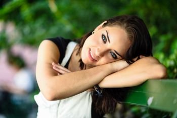 Happy young woman with blue eyes looking at camera sitting on urban bench Smiling beautiful girl with sweet look