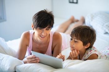 Funny mom and lovely little girl are having fun on the bed Middle-age mother with her eight years daughter using digital tablet in bedroom Middle-a