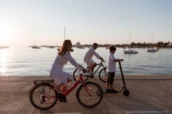 Happy family enjoying a beautiful morning by the sea together  parents riding a bike and their son riding an electric scooter Selective focus High-q