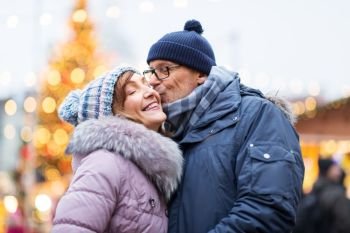 love  winter holidays and people concept - happy senior couple kissing at christmas market happy senior couple kissing at christmas market