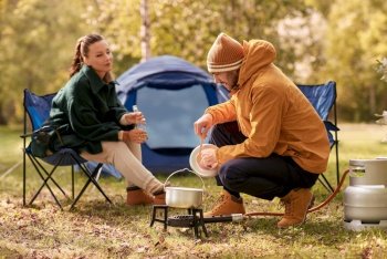 camping  tourism and travel concept - happy couple drinking beer and cooking food in pot on tourist gas burner at tent camp couple drinking beer and 