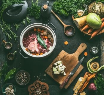 Raw meat in cooking pot on kitchen table background with vegetables   seasoning and kitchen utensils  top view Flat lay Meat dishes recipes Broth  
