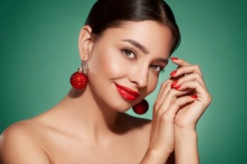 Portrait of beautiful young woman on green background  red lipstick and festive makeup  Christmas toy earrings  shiny glowing skin  Winter holidays co