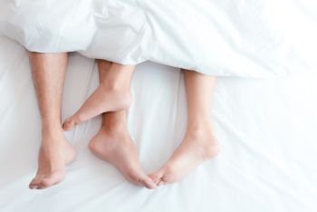 Closeup feet of couple on the bed Man and woman lovers make love under the blanket or bed sheet Sex on vacation theme Valentine and Honeymoon conce