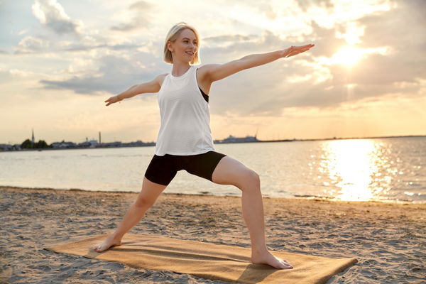 fitness sport and healthy lifestyle concept - happy woman doing yoga warrior pose on beach over sunset happy woman doing yoga warrior pose on beach