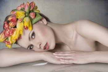 close-up portrait of sexy blonde girl with spring look posing lying on table with naked shoulders  colorful make-up and floral garland