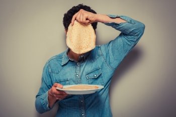 Young man is hiding his face behind a pancake