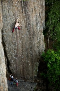 A male climber against a large rock face climbing lead