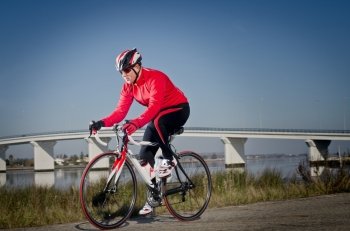 Man on road bike riding down open country road  bridge on background