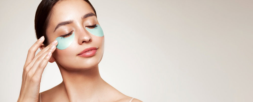 A young beautiful smiling woman with cosmetic patches on her eyes Cosmetic procedures skin care around the eyes Perfect healthy facial skin A young beautiful smiling woman with cosmetic patches on her eyes Cosmetic procedures skin care around the eyes Perfect healthy facial skin