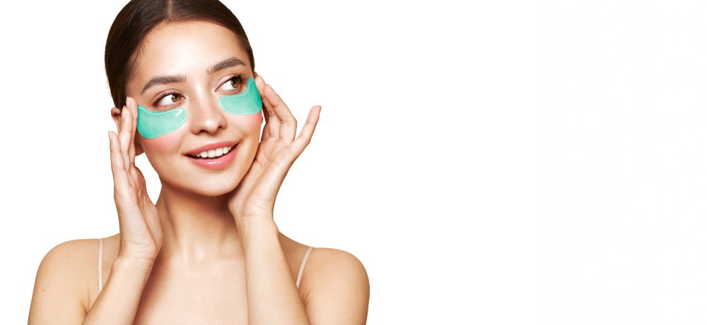 A young beautiful smiling woman with cosmetic patches on her eyes Cosmetic procedures skin care around the eyes Perfect healthy facial skin A young beautiful smiling woman with cosmetic patches on her eyes Cosmetic procedures skin care around the eyes Perfect healthy facial skin
