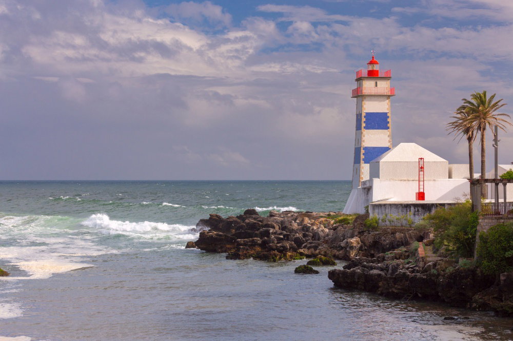 Santa Marta Lighthouse stands on the rocky Atlantic coast with waves and palm trees in Cascais Portugal Santa Marta Lighthouse on Rocky Coast in Ca Santa Marta Lighthouse stands on the rocky Atlantic coast with waves and palm trees in Cascais Portugal Santa Marta Lighthouse on Rocky Coast in Ca