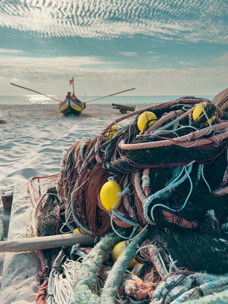 Traditional fishing net with yellow floats piled on sandy beach with a colorful arte xavega boat and blue cloudy sky in Portugal Traditional fishing net with yellow floats piled on sandy beach with a colorful arte xavega boat and blue cloudy sky in Portugal